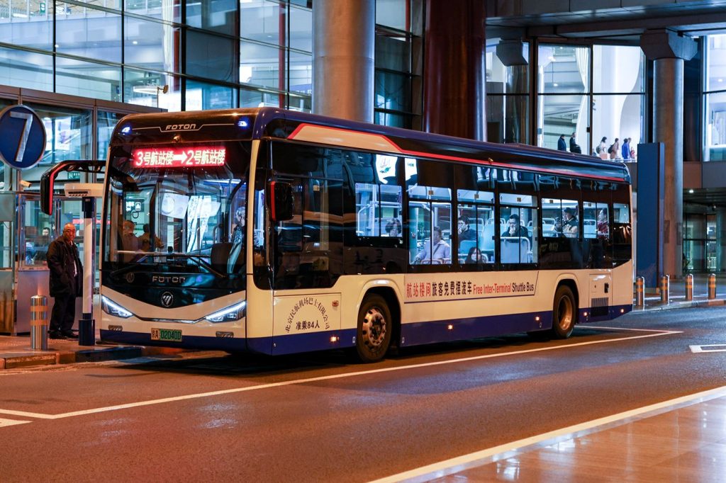 Passengers board an airport shuttle bus outside a busy modern terminal.